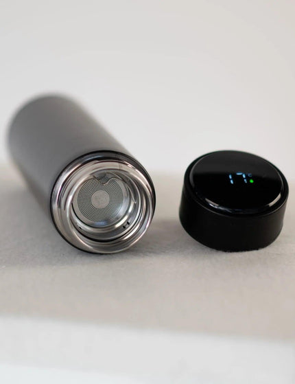 Gourde isotherme noire Obéna avec affichage LED de température et filtre à thé intégré, posée sur une surface minimaliste.