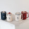 Collection de mugs isothermes Obéna en trois couleurs : bleu nuit, beige et rouge, posés sur un socle blanc.