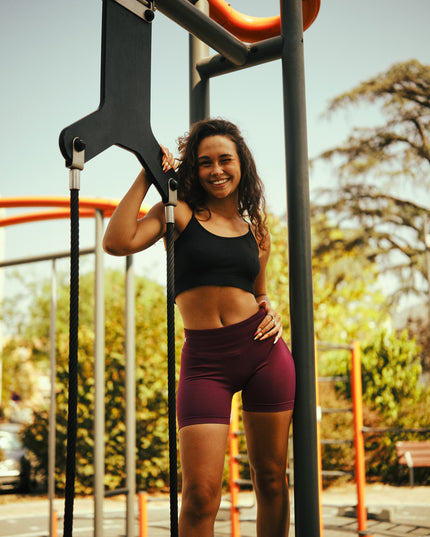 Femme souriante portant le short de sport Obéna violet Aura, debout en extérieur près d’un équipement de street workout.