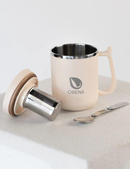 Tasse isotherme Obéna avec couvercle hermétique et filtre en acier inoxydable, accompagnée de cuillères en inox, posée sur une surface minimaliste.